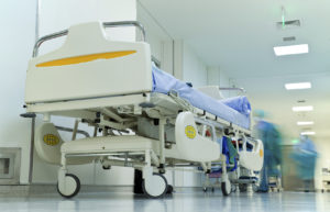 Empty bed in busy hospital corridor, blurred figures with medical uniform working